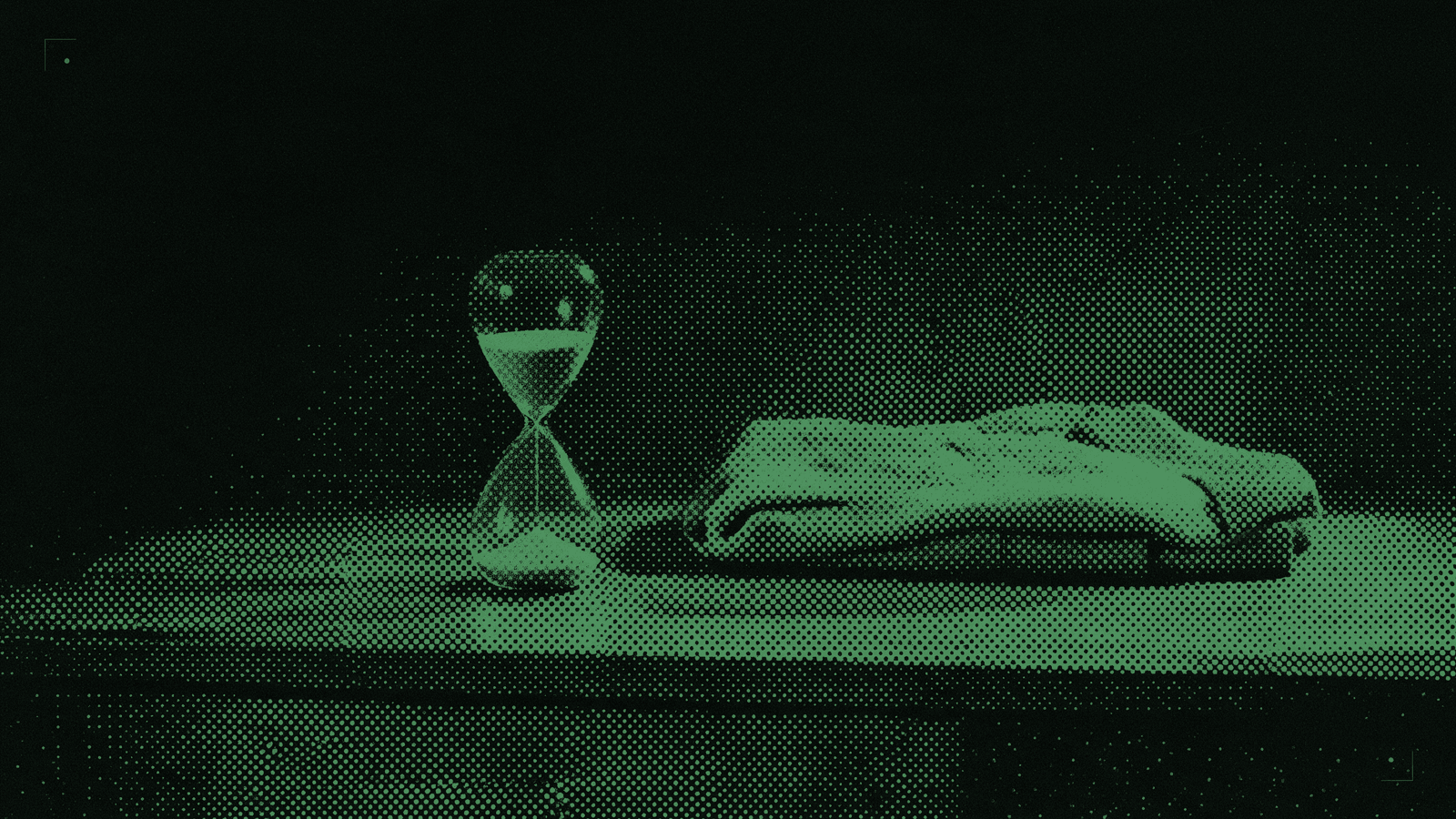 A small hourglass with sand mid-fall beside one folded garment on a bare counter