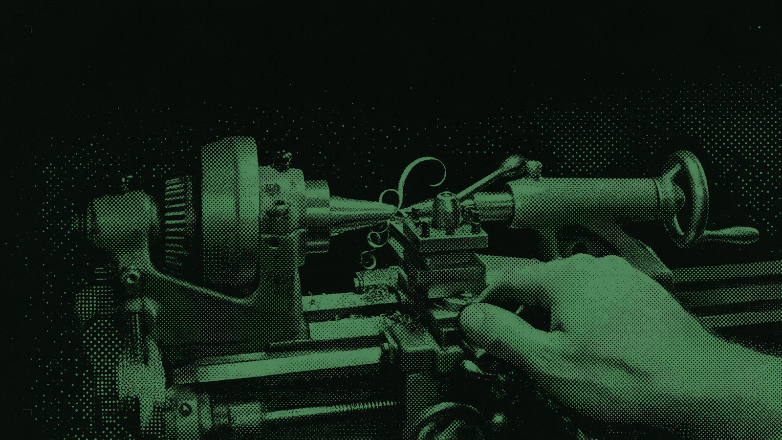 A machinist's hand steadying the tool post of a running lathe while one long chip curls off the cutting edge